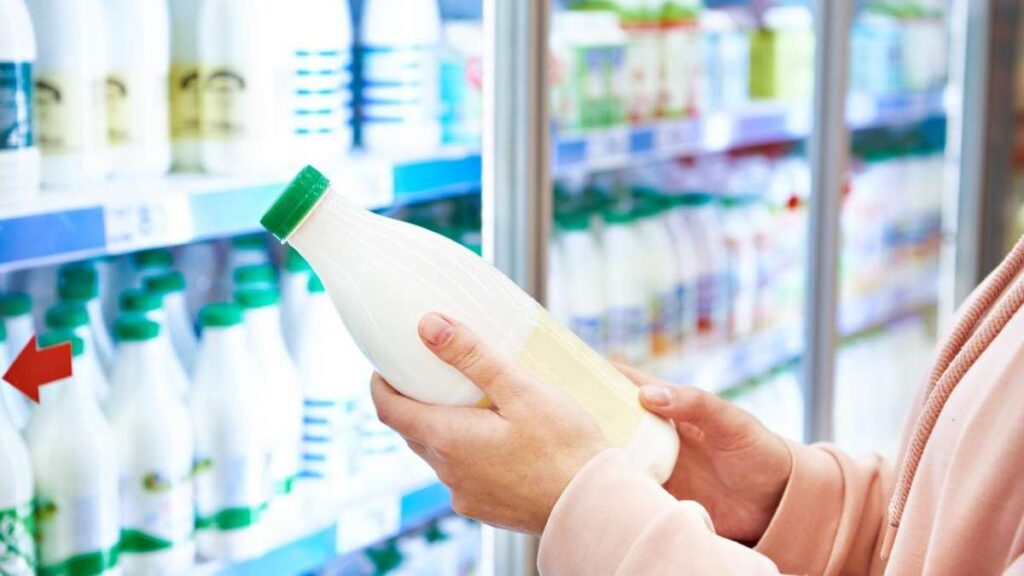 La imagen muestra a una persona examinando una botella de leche en una tienda, destacando la importancia de la transparencia en el etiquetado y la información nutricional para los consumidores actuales.